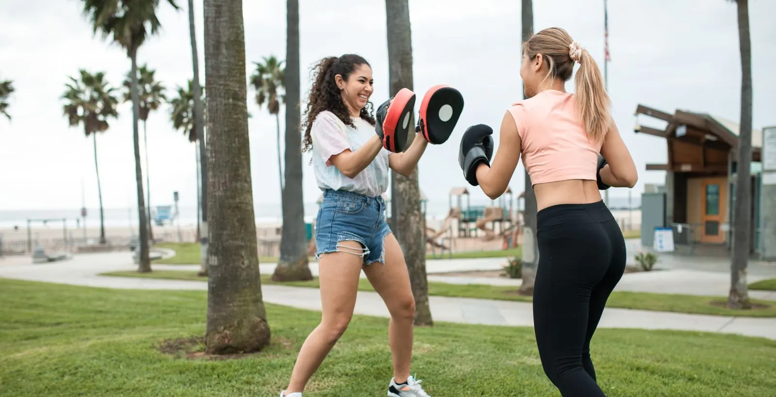 A trainer holds pads for a client during an outdoor boxing session