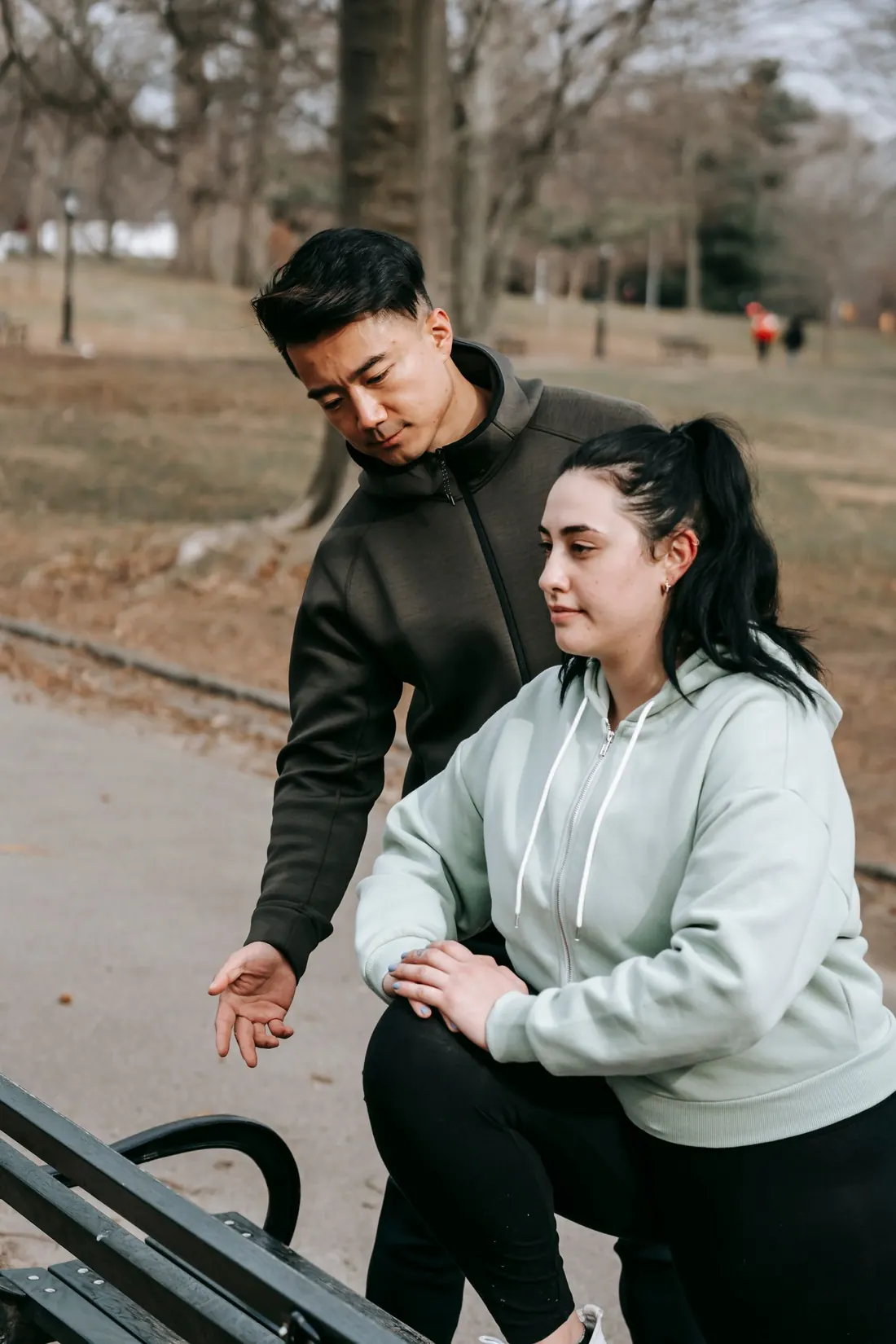 A trainer shows a client how to do a step-up on a park bench