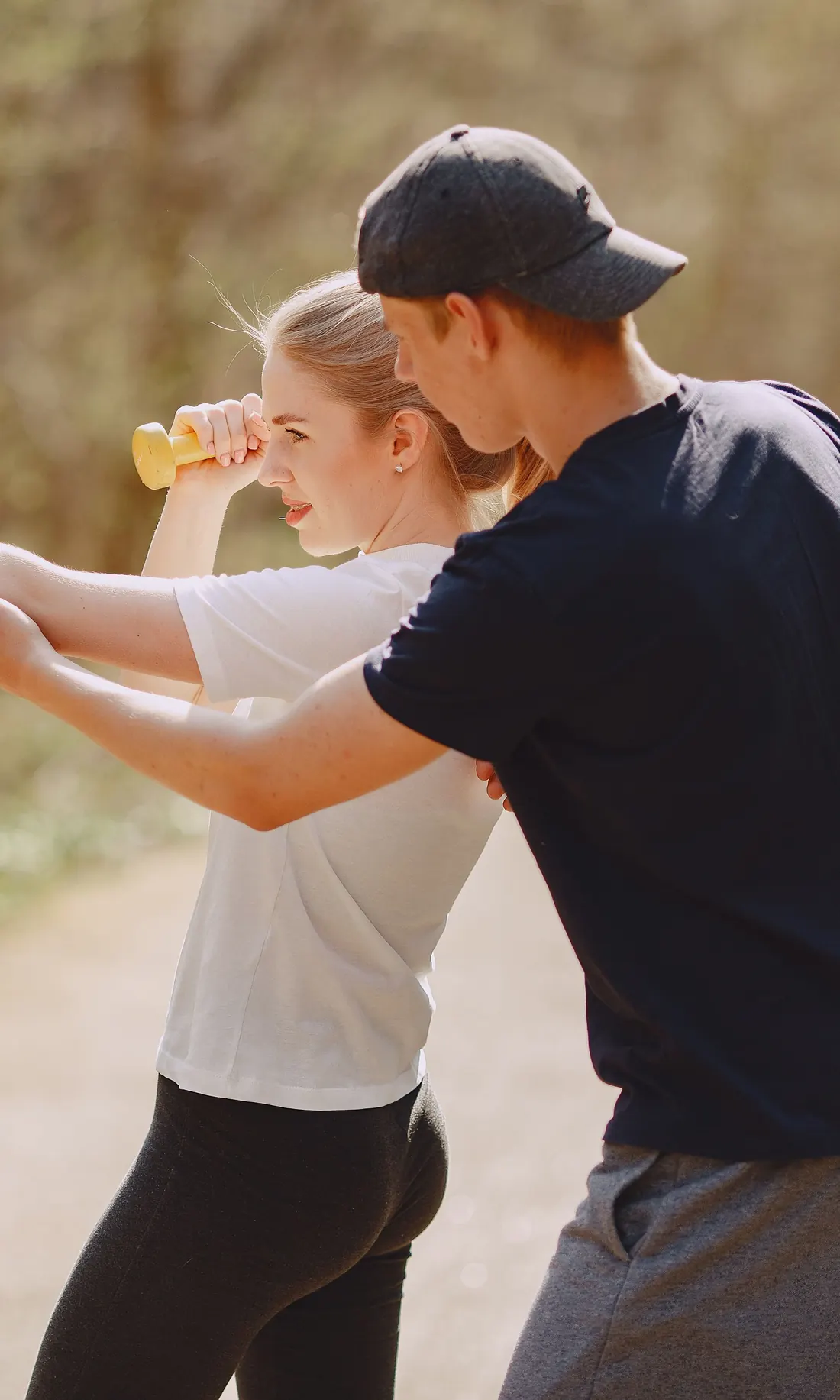 A trainer guides a client through a dumbbell exercise on a park path