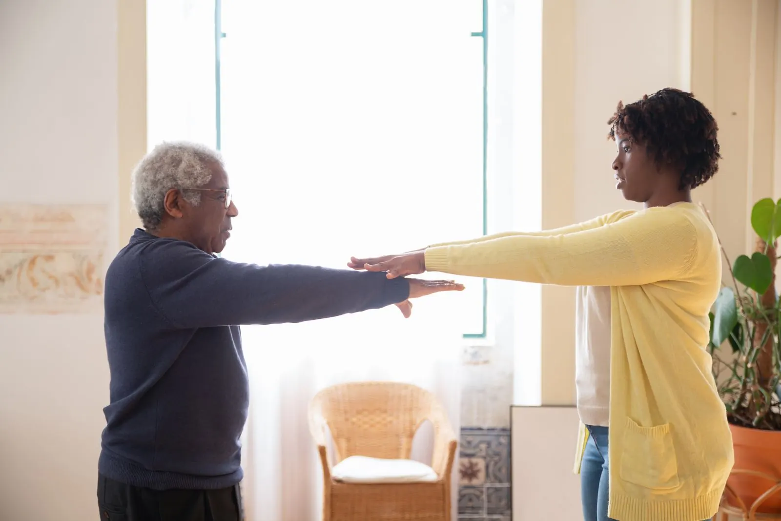 A trainer leads an older client through an arm exercise at home