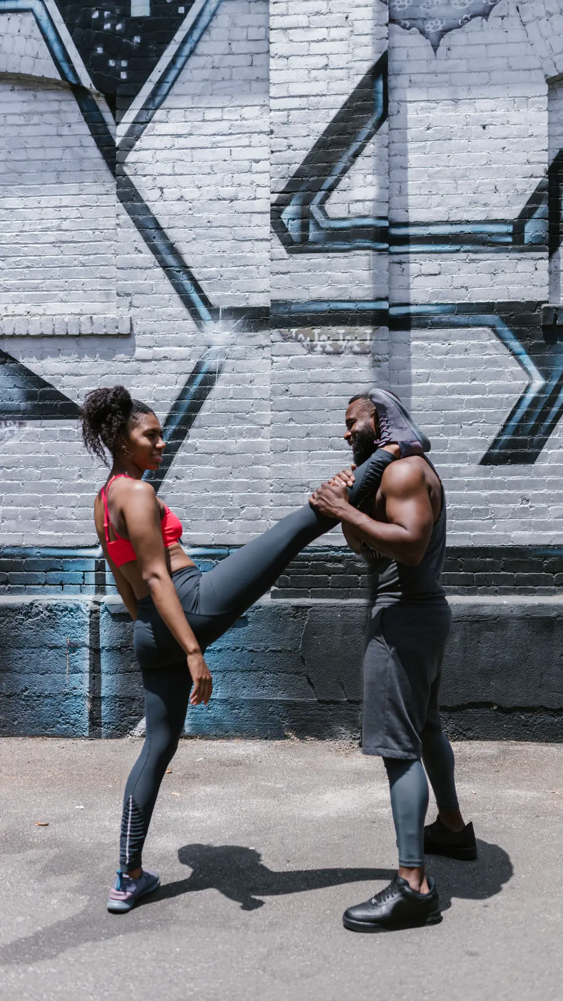 A trainer and client smiling together against a city wall