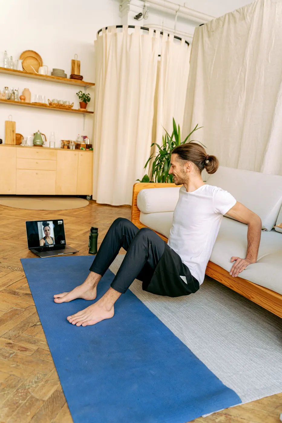 A man exercising on a mat at home with a tablet propped up in front of him showing a video call