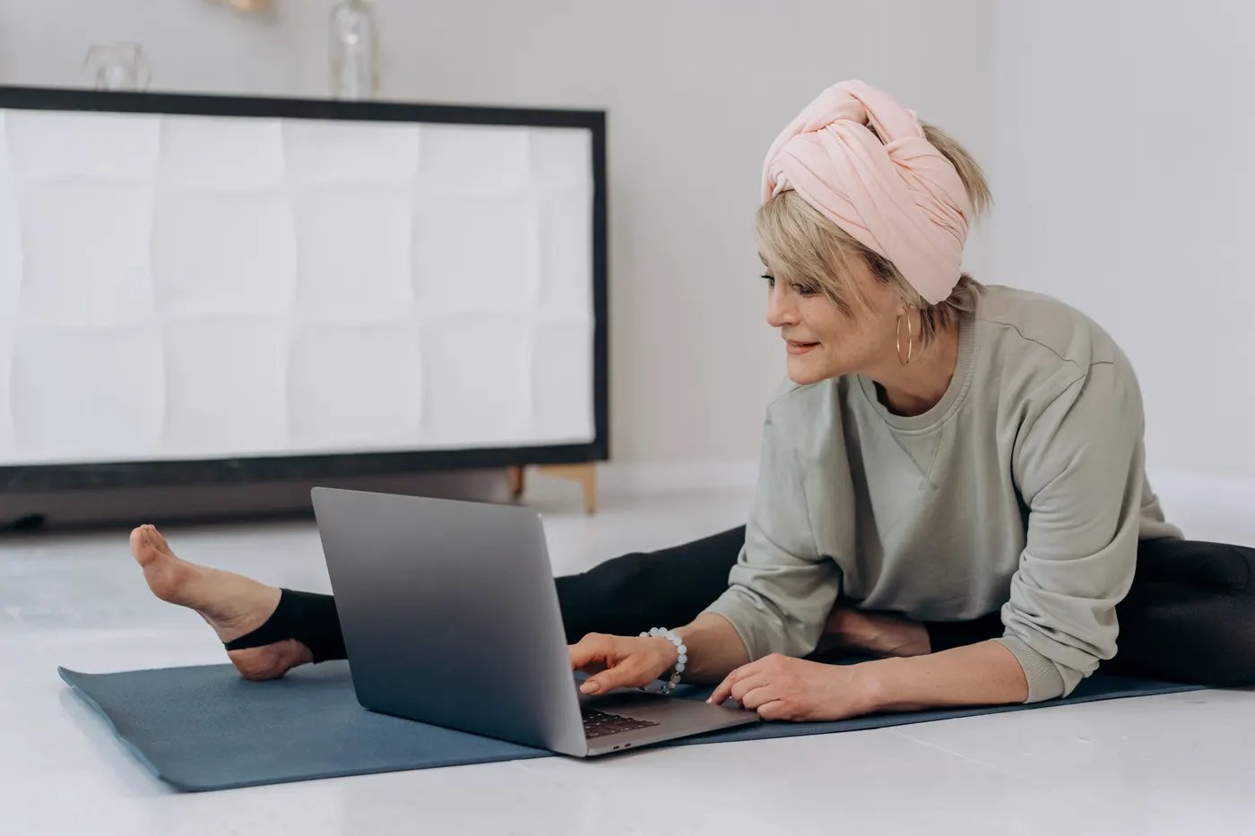 A woman stretching on a mat at home while following a session on her laptop