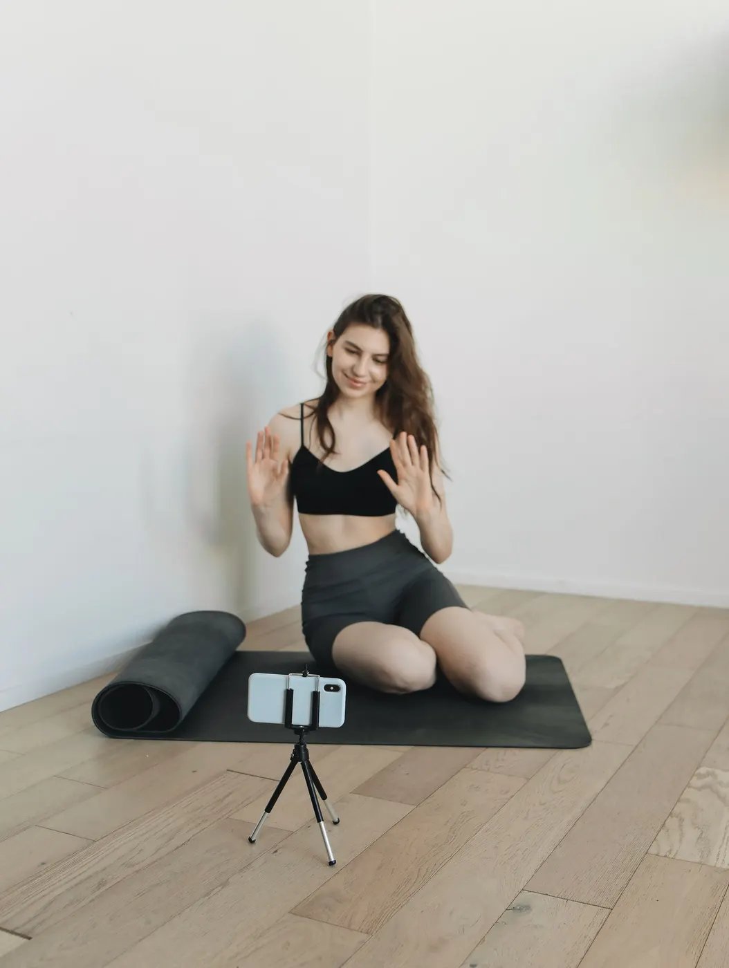 A woman on a mat at home waving at her phone on a small tripod