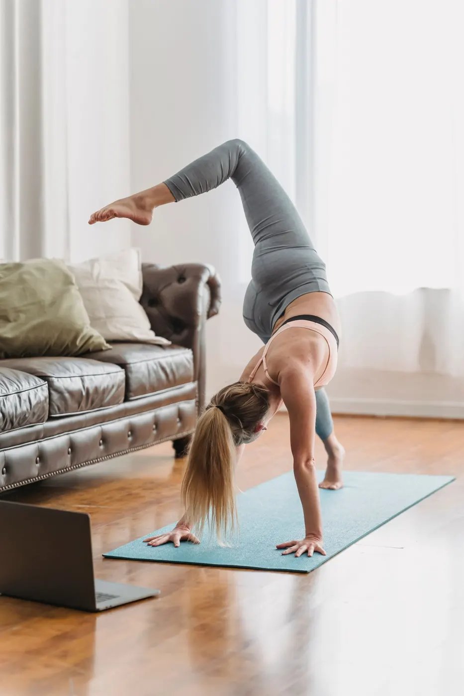 A woman doing a yoga pose on a mat in her living room with a laptop open on the floor
