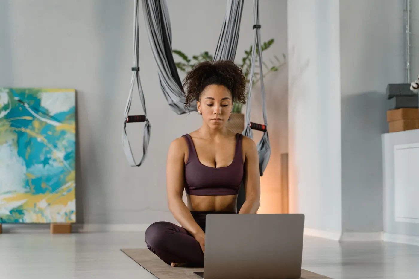 A woman sitting cross-legged on a mat at home, following a session on her laptop