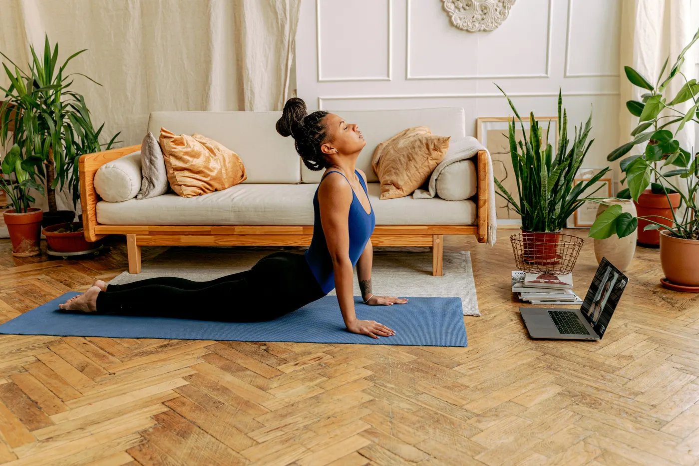 A woman doing a cobra stretch on a mat in her living room, following a session on a laptop on the floor
