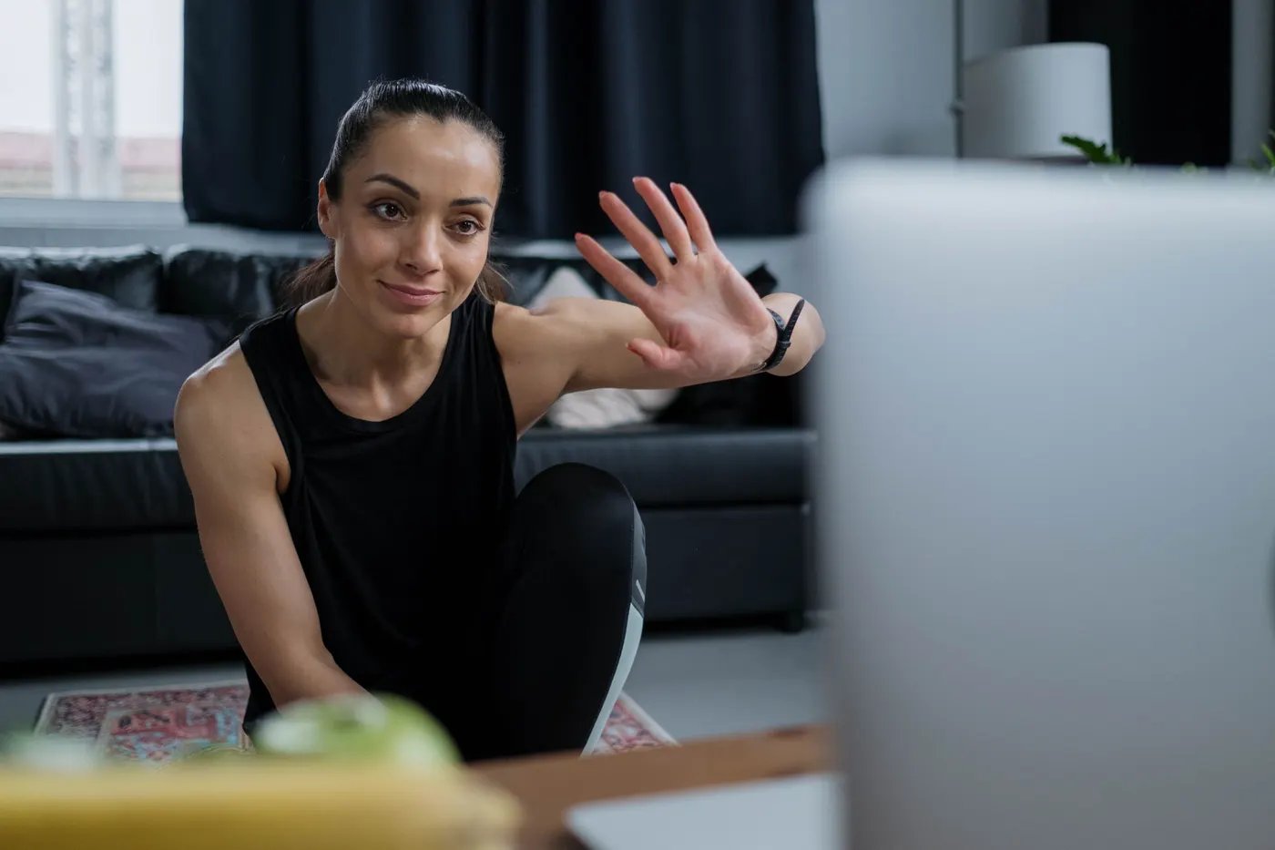 A woman on a mat at home waving at her trainer on a video call