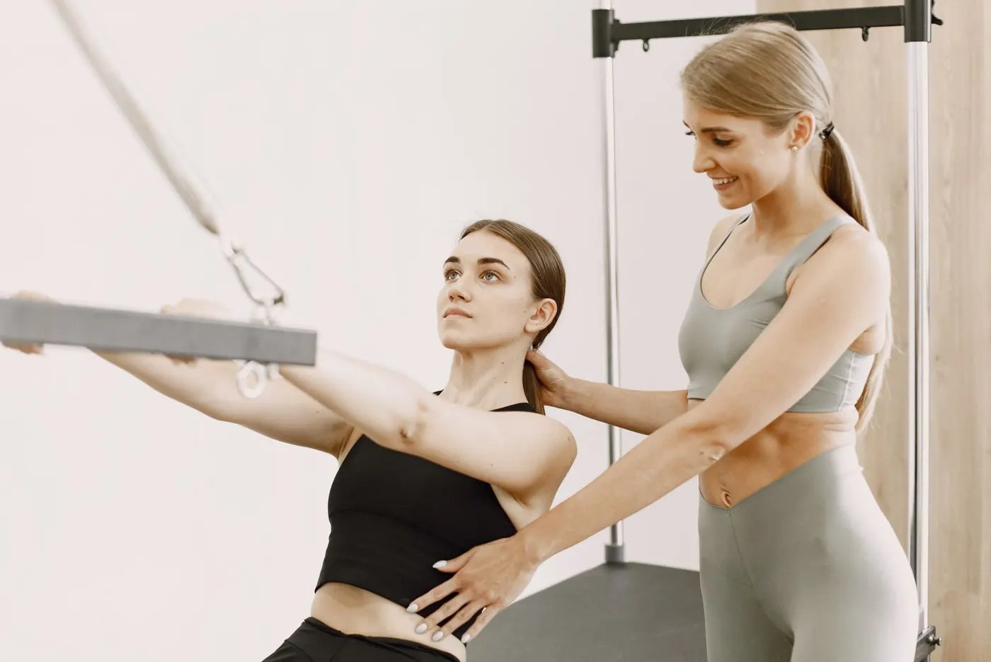 A trainer supporting a woman's arm as she pulls a cable handle in a studio