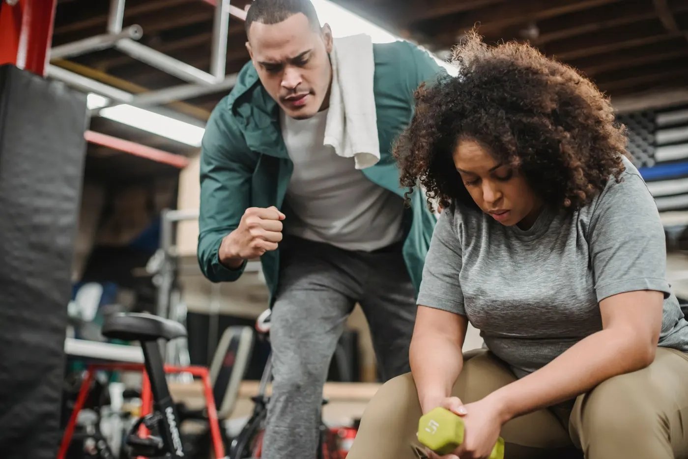A trainer guiding a woman through a dumbbell exercise in a private gym