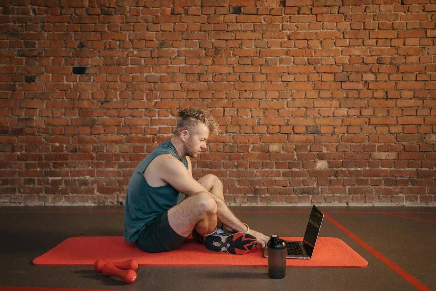 A man stretching on an orange mat with a laptop open beside him