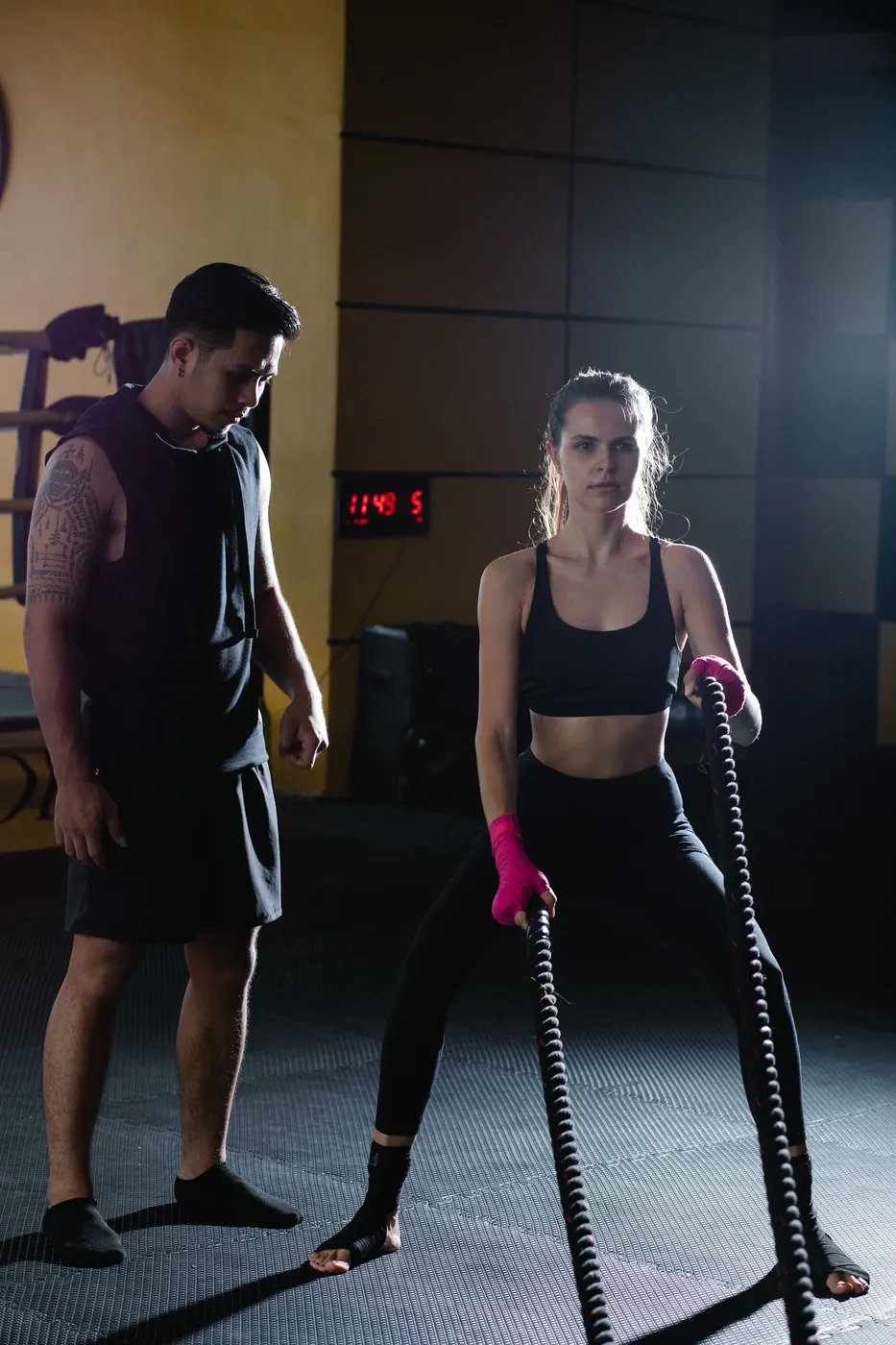 A personal trainer watching closely as a woman works through a battle rope set