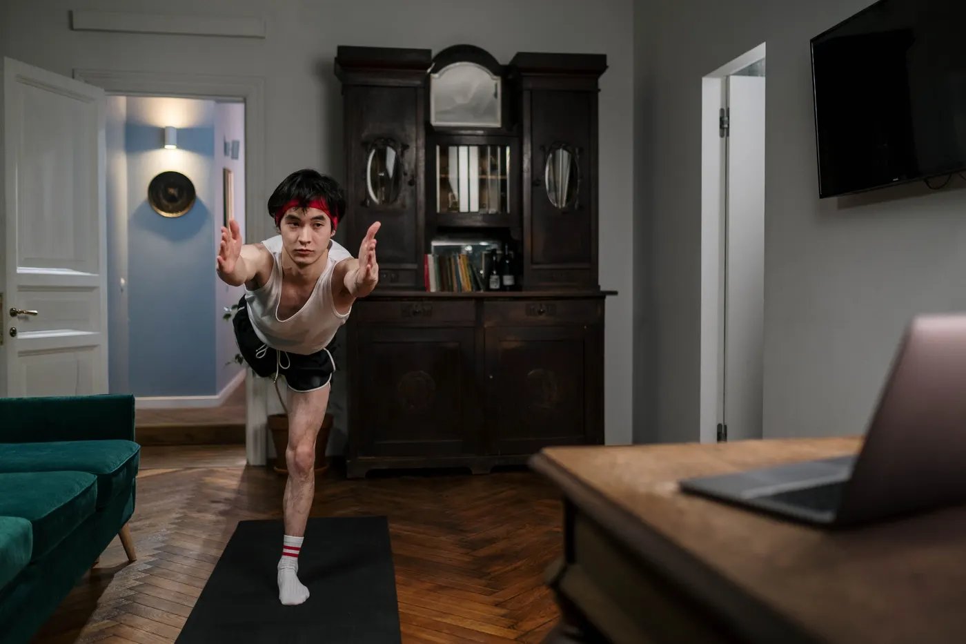 A man balancing on one leg in his living room with a laptop open on the table